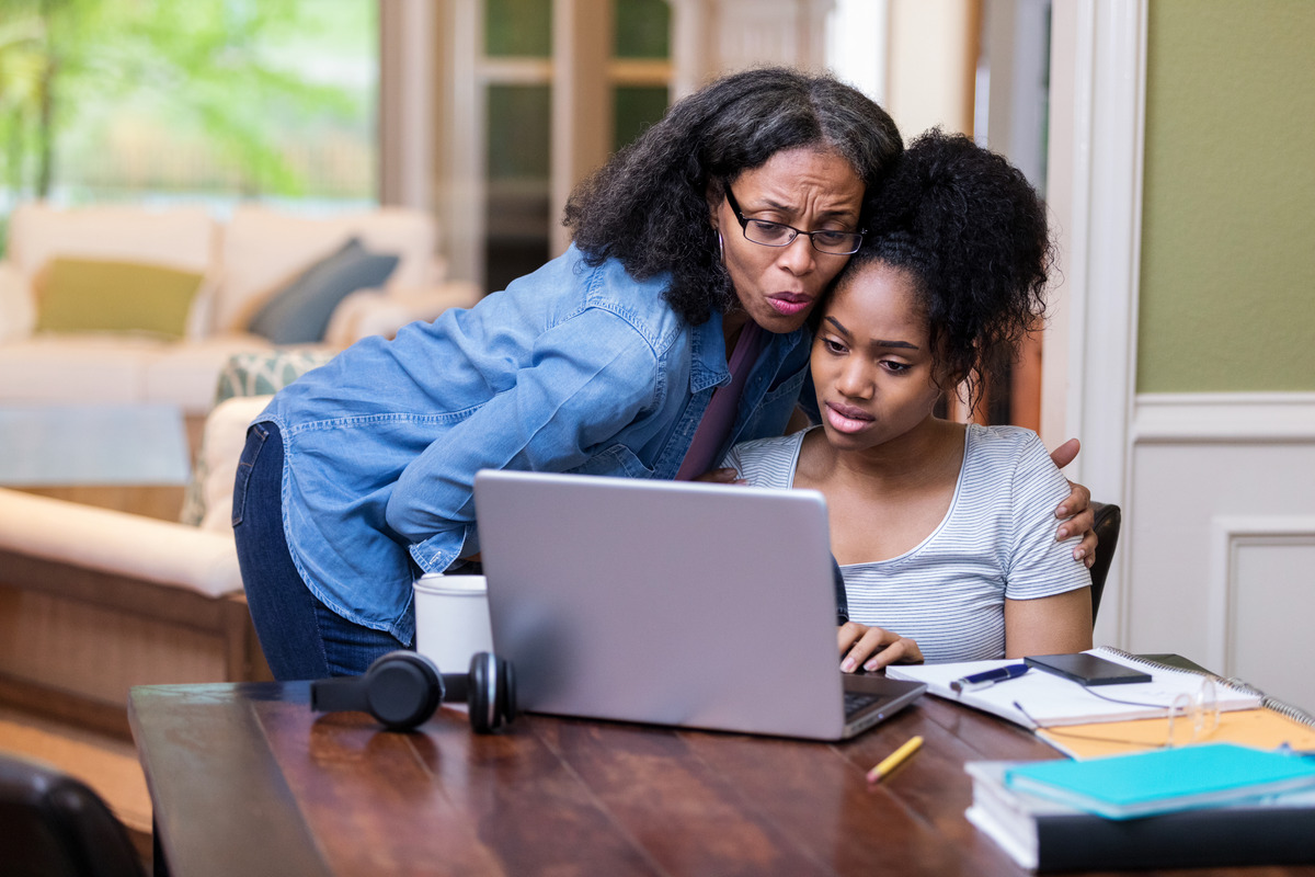 student sitting at computer receiving hug from mom